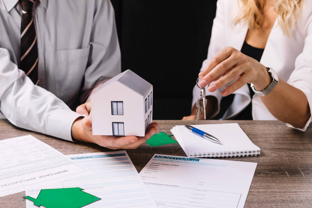 Das Bild zeigt ein paar mit einem Haus und Hausschlüssel in der Hand. Es steht symbolisch für den An- und Verkauf als Bewertungsanlass der Immobilienvbewertung